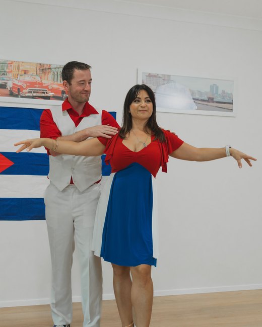Nikoletta with her arms open, dancing with Stephen in front of a Cuban flag