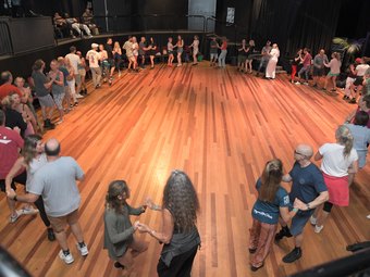 A large rueda circle of couples on a wooden dance floor